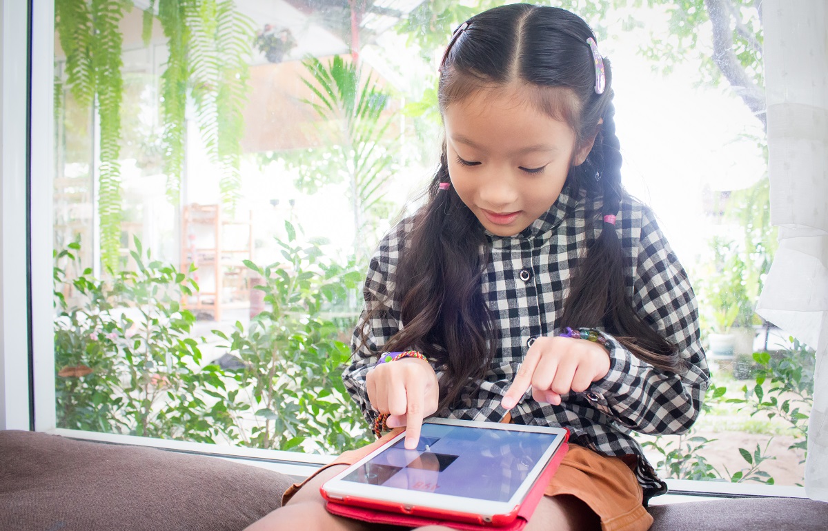 You girl sitting by a window using a touchscreen tablet device
