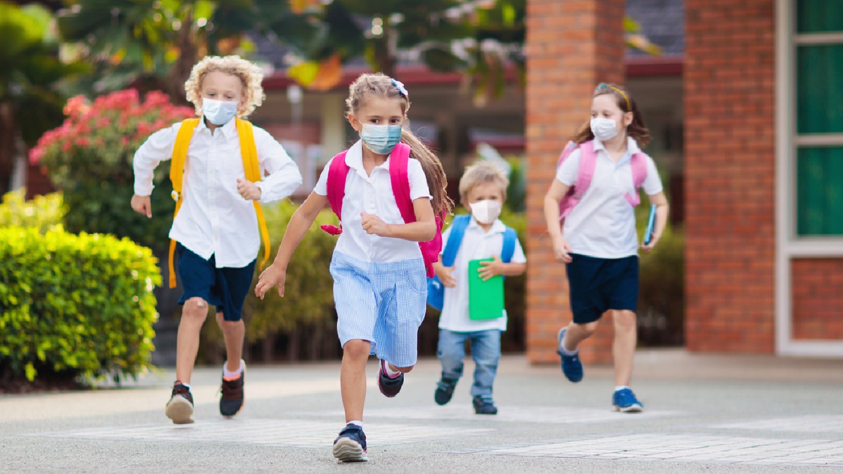 School children with face masks run into school with backpacks on