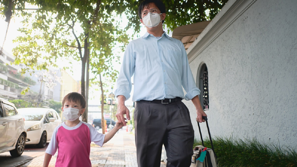 Father and child walking on street holding hands wearing face masks
