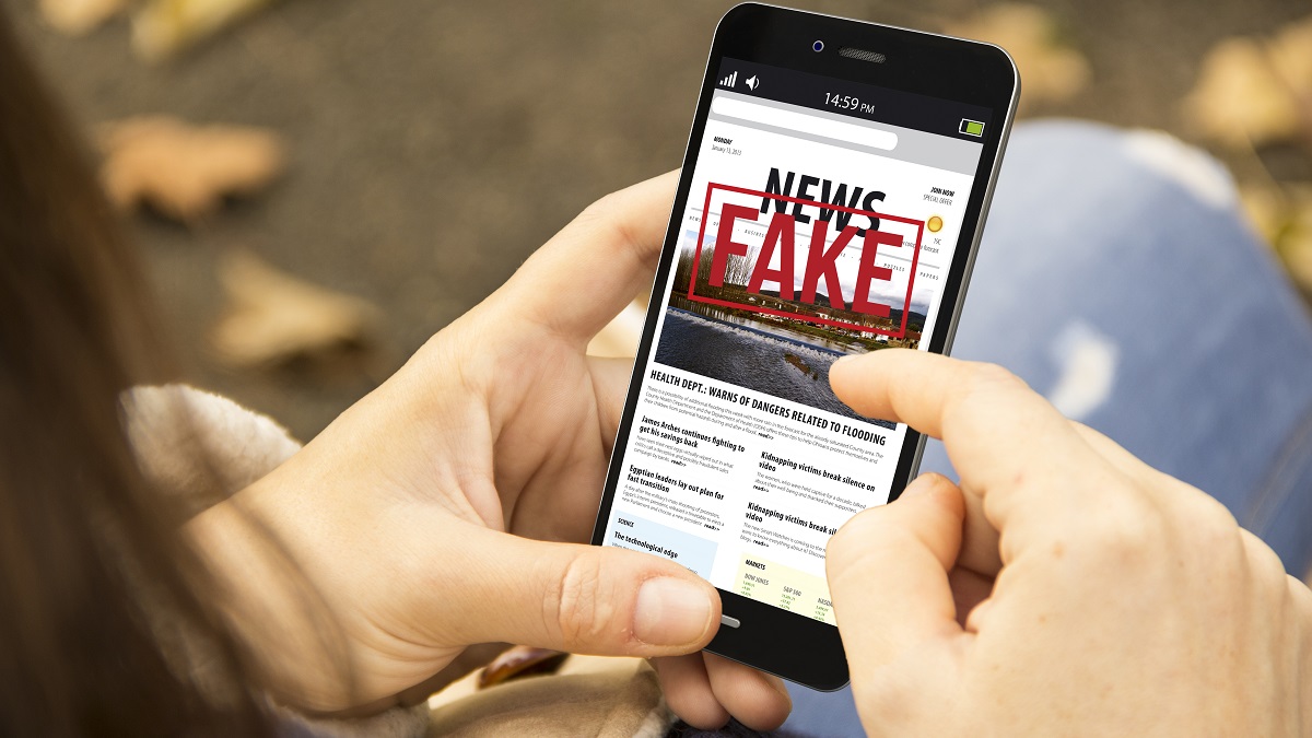 Person holding smart phone with words "fake news" on the screen