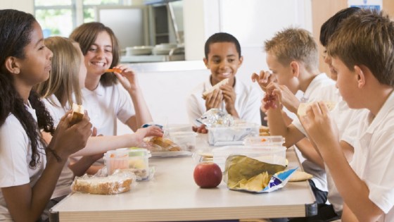 School children at a table in cafeteria eating lunch together