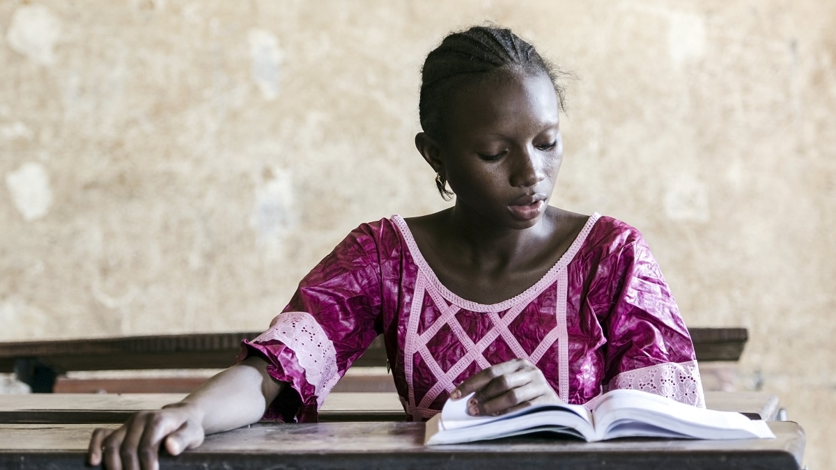 Young African girl sitting at a desk in a classroom reading a book