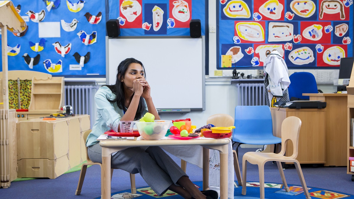 Female teacher in classroom sitting at table looking stressed