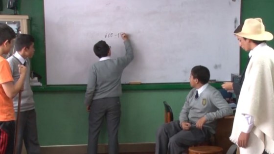 Colombian classroom scene with student writing on whiteboard while teacher and other students watch