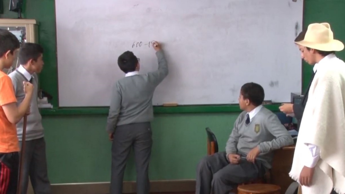 Colombian classroom scene with student writing on whiteboard while teacher and other students watch