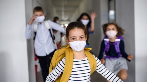School children wearing face masks in school corridor running towards the camera