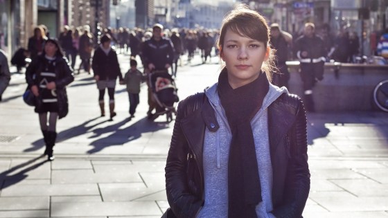 Woman looking into camera stands alone on a busy shopping street