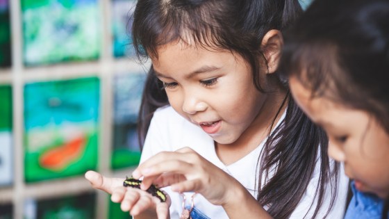 Young girl looks curiously at a caterpillar in her hand