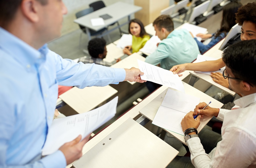 Teacher hands exam paper to student in lecture theatre
