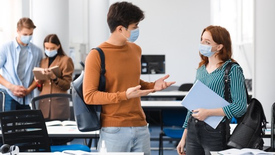 University students standing in a classroom with face masks on, talking with each other