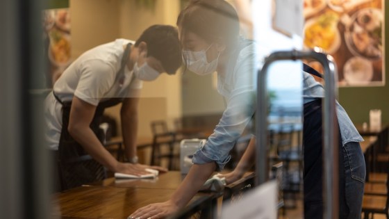 Waiter wearing protective face mask while cleaning tables in restaurant