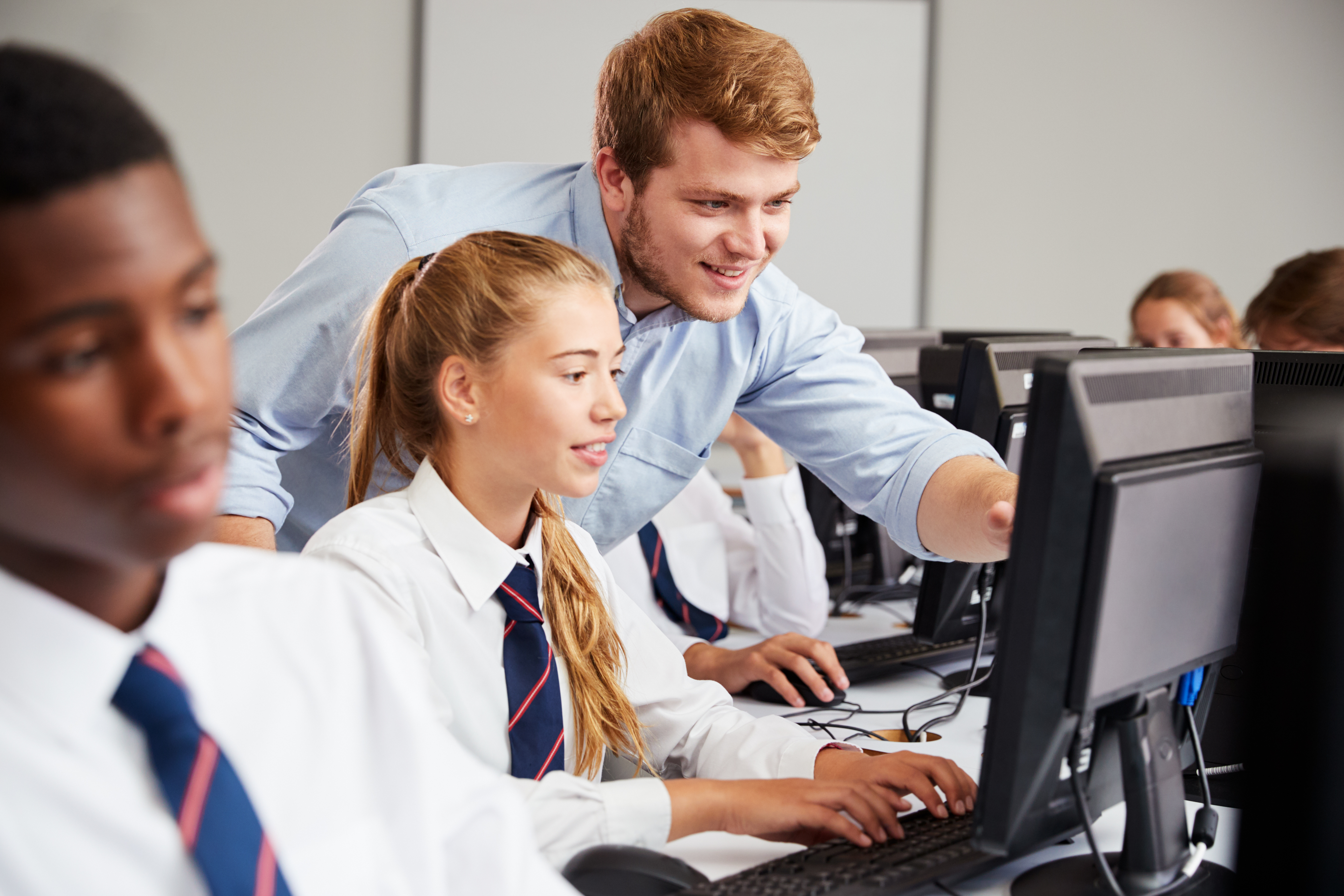 Teenage students in class with computers, teacher explaining